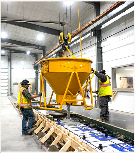 Workers pouring concrete from an overhead bucket on a precast site